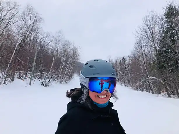 Adrienne Clarke, seen from the chest up, wearing ski goggles and helmet while skiing outside