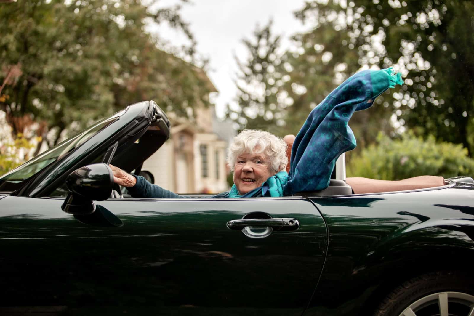 Judy Carson is in the driver’s seat of a green convertible. Her scarf flowing in the wind.