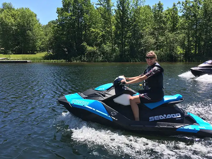 Sarah Petrie, on a jetski. A lake and trees can be seen behind her
