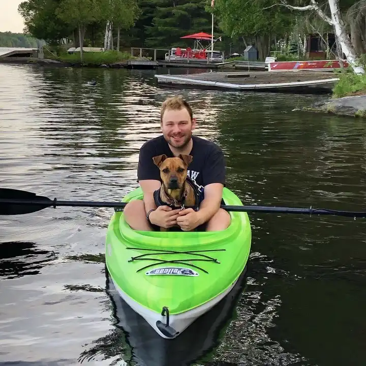 Steve Smyth, posing for a photo in a kayak while his dog sits in front of him
