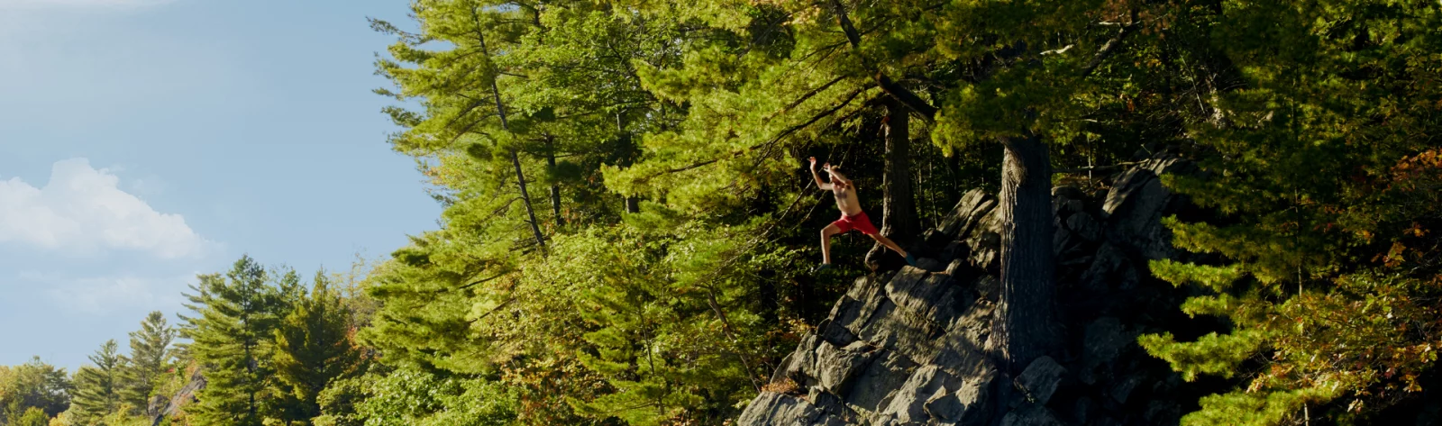 A man leaps into a clear lake from an overhanging cliff